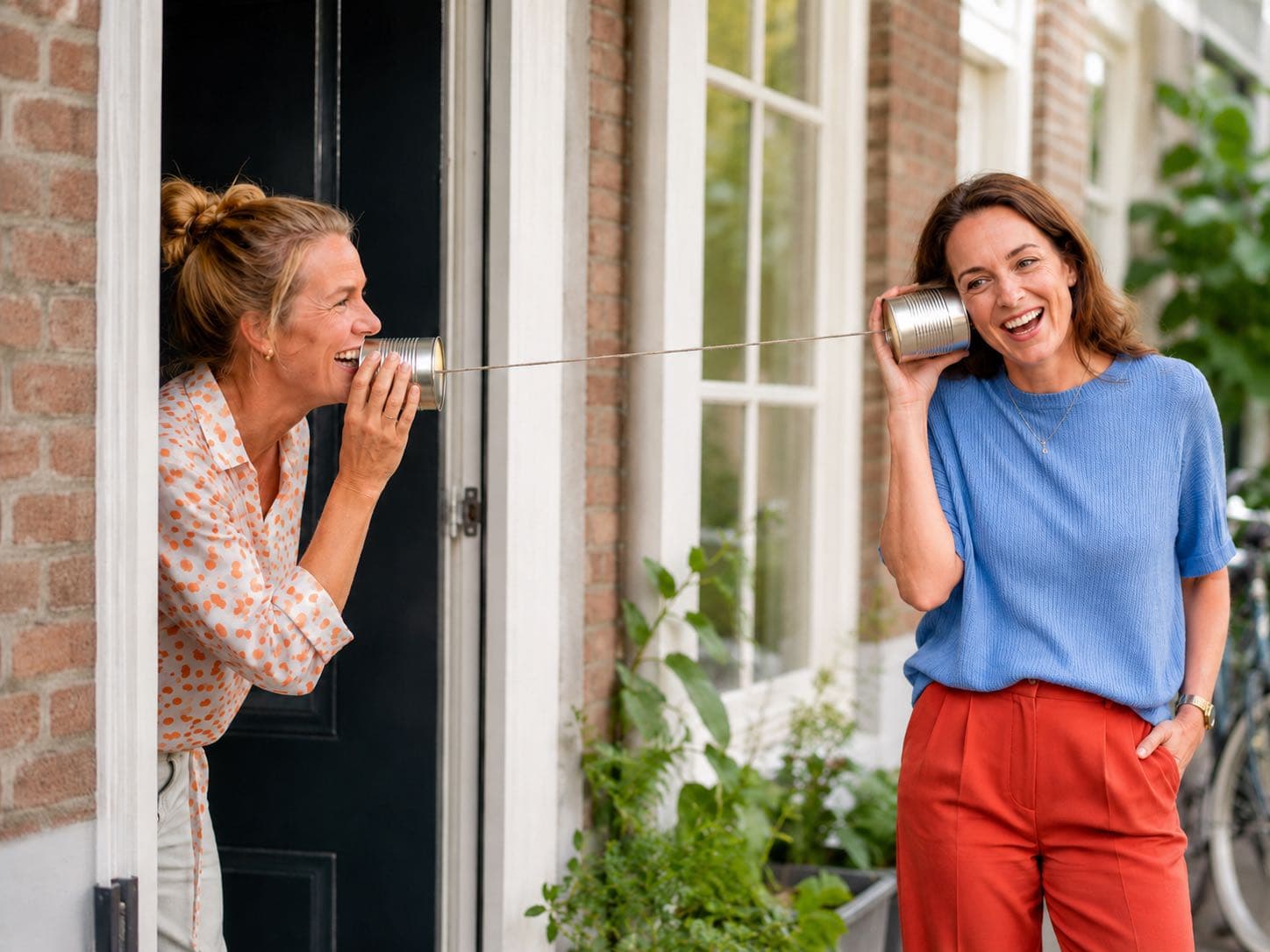 Twee vrouwen praten met elkaar via blikken die met een touwtje verbonden zijn.